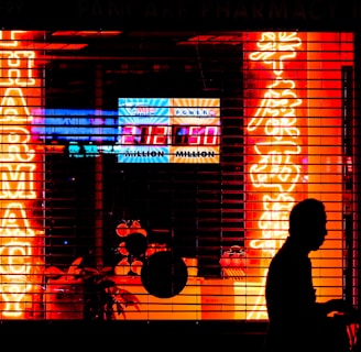 Bright neon signs in orange and yellow light up the storefront of a pharmacy, visible through metal security bars. The silhouette of a person walking by is prominent in the foreground, set against the vibrant colors. Additional signage displays a lottery number in bright white and blue.