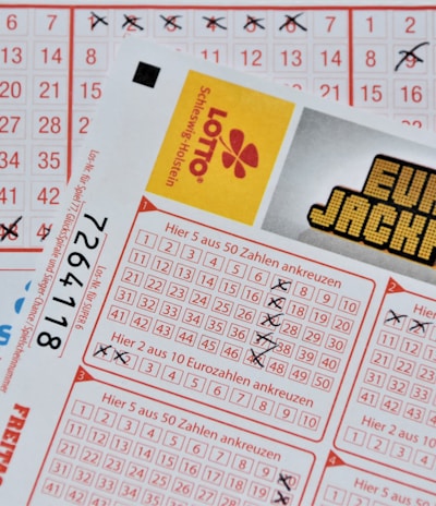 Three lottery tickets are displayed, including Eurojackpot and Super 6. Various numbers are marked on the tickets, with some crossed out and others checked. The Eurojackpot ticket is partially visible with the logo prominently displayed, and a ticket number is visible on one of the tickets.