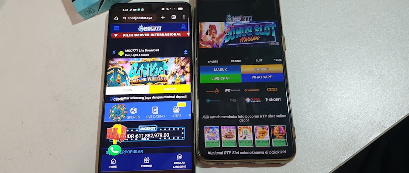 Two smartphones are displayed on a white surface, both showing gambling websites with colorful graphics, text, and various options for logging in and accessing games. The screens are bright and filled with promotional content related to casino and slot games.